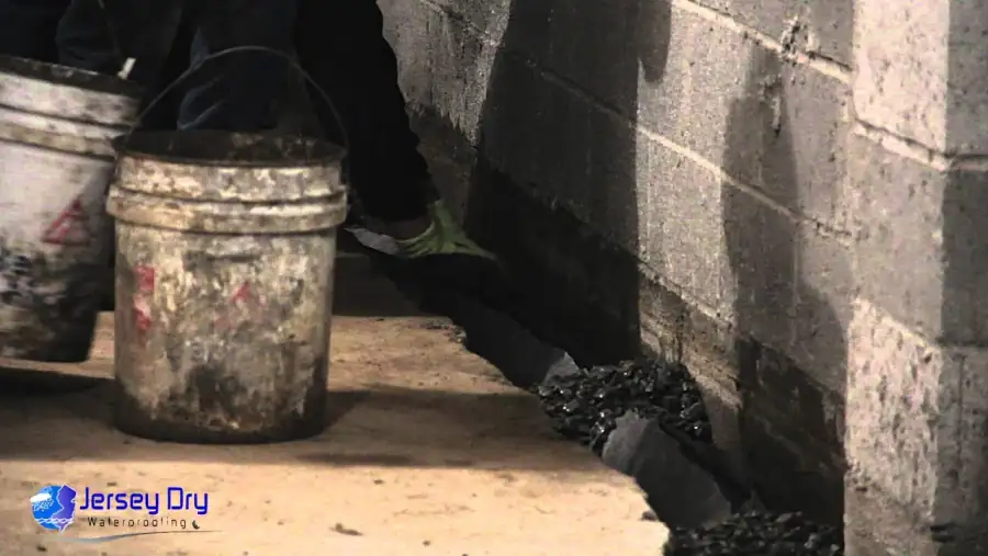 Jersey Dry technician setting stone into an interior perimeter drain trench in a block-wall basement