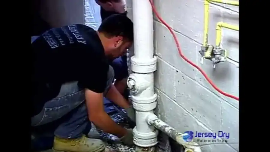 Two Jersey Dry technicians connecting a sump pump discharge line in a basement